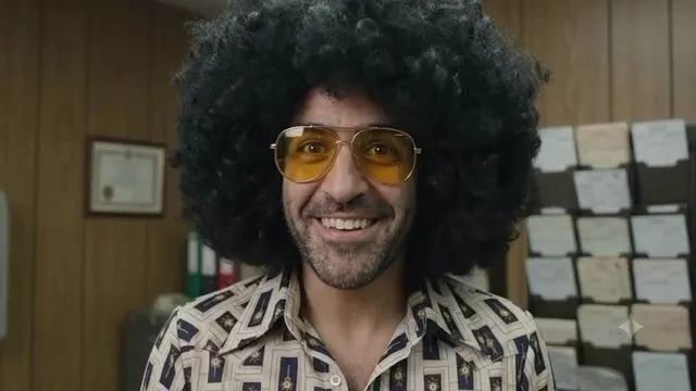 דמות עם שיער אפרו ומשקפי שמש צהובים במשרד — פריים מסרטון פרסומת